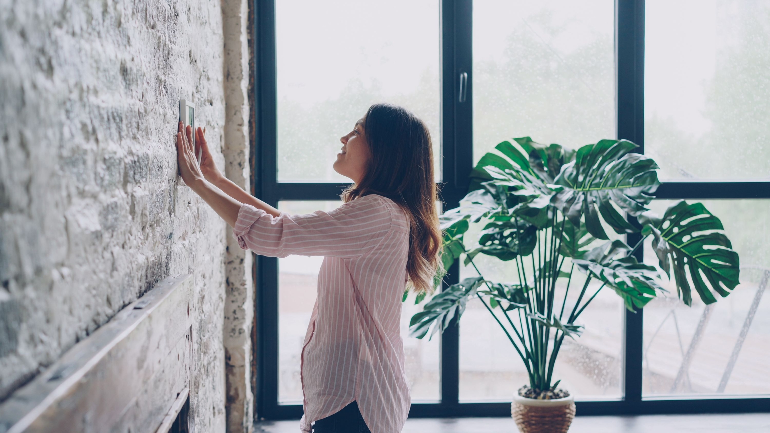 Femme réglant un thermostat connecté mural pour piloter le chauffage de son logement